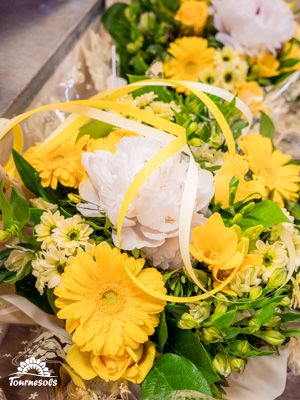 Bouquet de fleurs fraîches jaunes et blanches avec gerberas, feuillage vert et ruban décoratif.